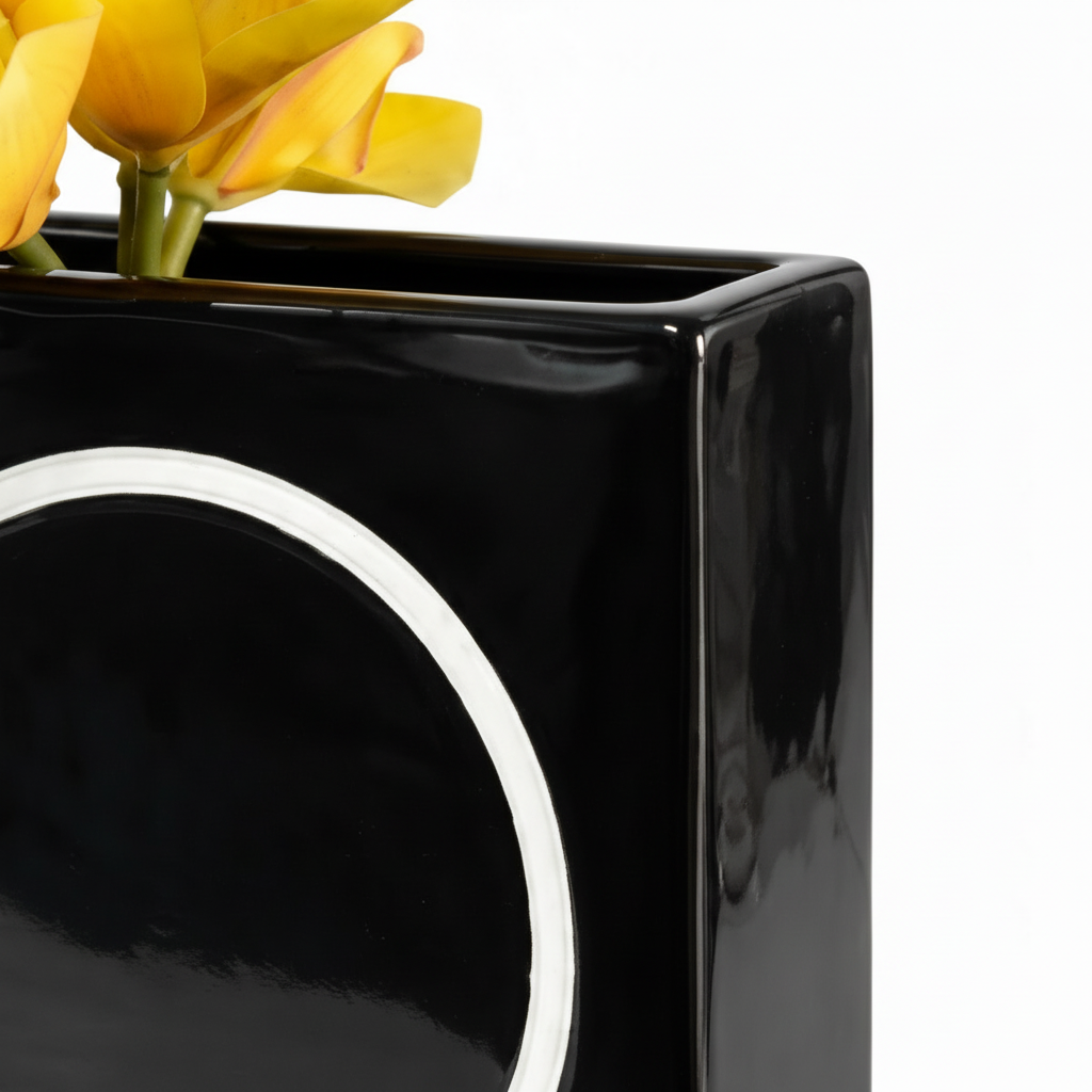 Close-up detail of glossy black ceramic vase with white circular accent